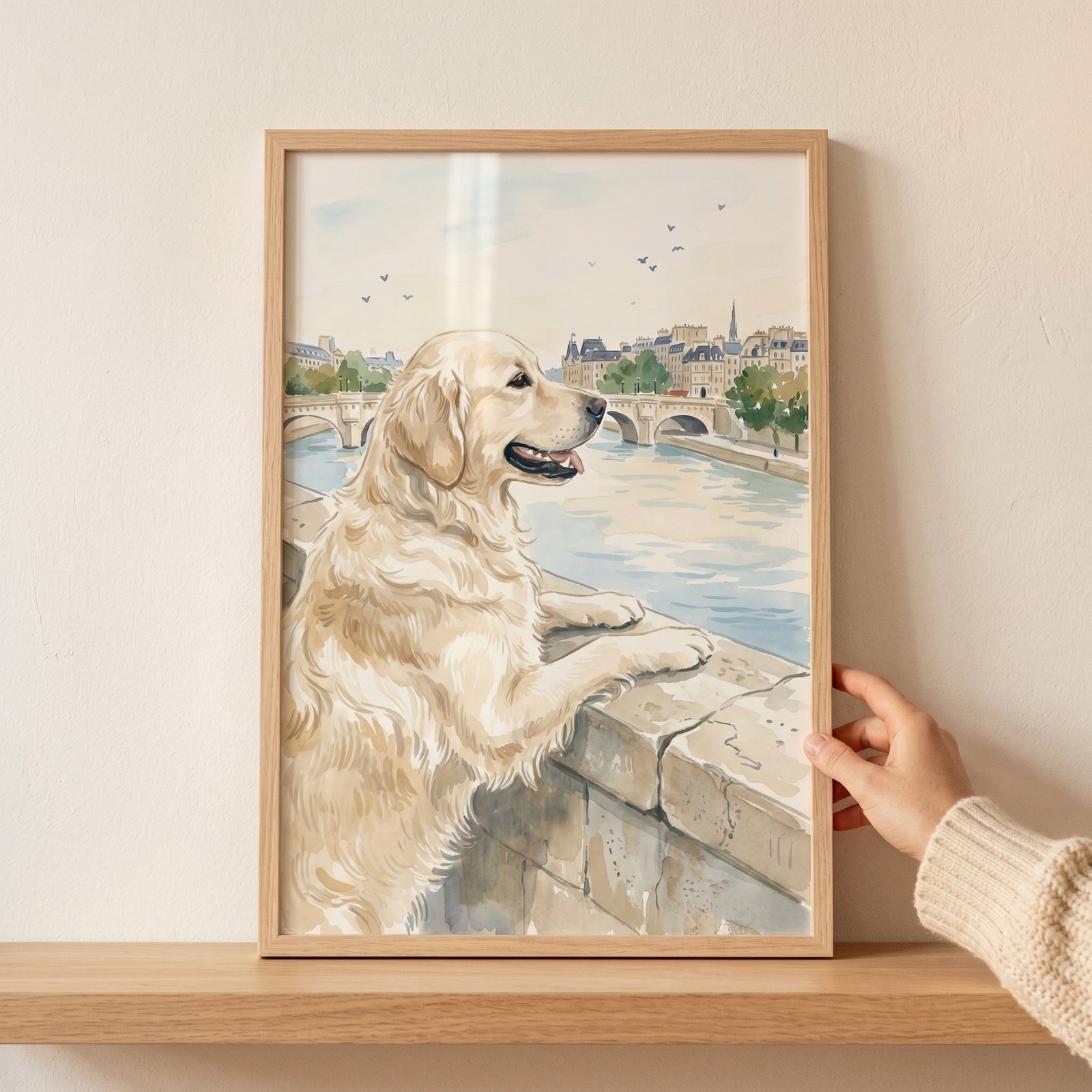 Hand holds vintage parisian golden retriever wall art of a dog looking over a river and city bridge.