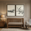 A sophisticated nursery features a neutral color palette and classic design elements. Centered on a taupe paneled wall are two large, black-framed sketches of vintage propeller aircraft. Below the artwork sits a sturdy wooden crib in a medium brown finish with a white mattress. To the left, a matching wooden side table holds a simple lamp with a beige shade and a small stack of books. To the right, a wooden rocking chair is draped with a textured cream-colored throw blanket. 