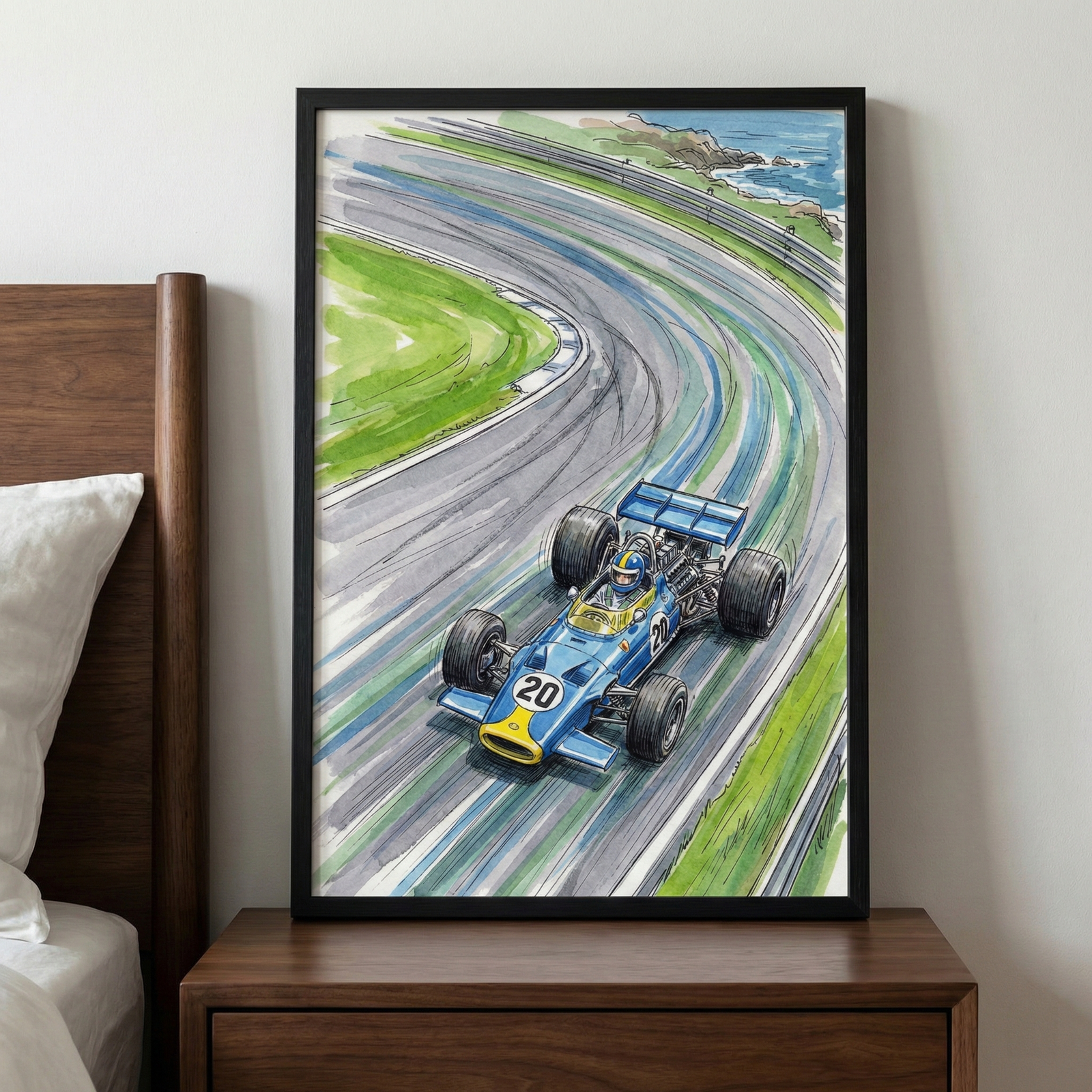A framed hand-drawn illustration of a blue vintage-style open-wheel race car speed around a sweeping curve on a racetrack. The vehicle features the number 20 in white circles and yellow accents on the front. The track is rendered with dynamic motion lines, bordered by bright green grass, with a glimpse of a blue sea and rocky coastline in the distance. The artwork is encased in a simple black frame and is displayed on a wooden nightstand next to a bed.