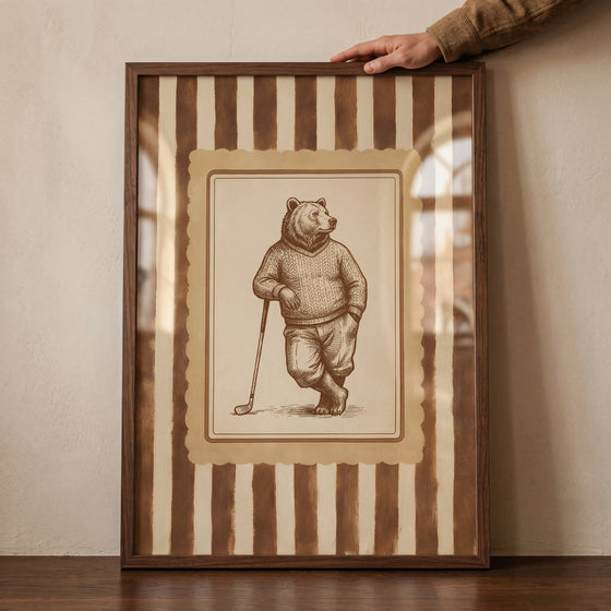 Framed vintage sepia golfing bear wall art depicts a bear in a sweater leaning on a golf club against vertical stripes.