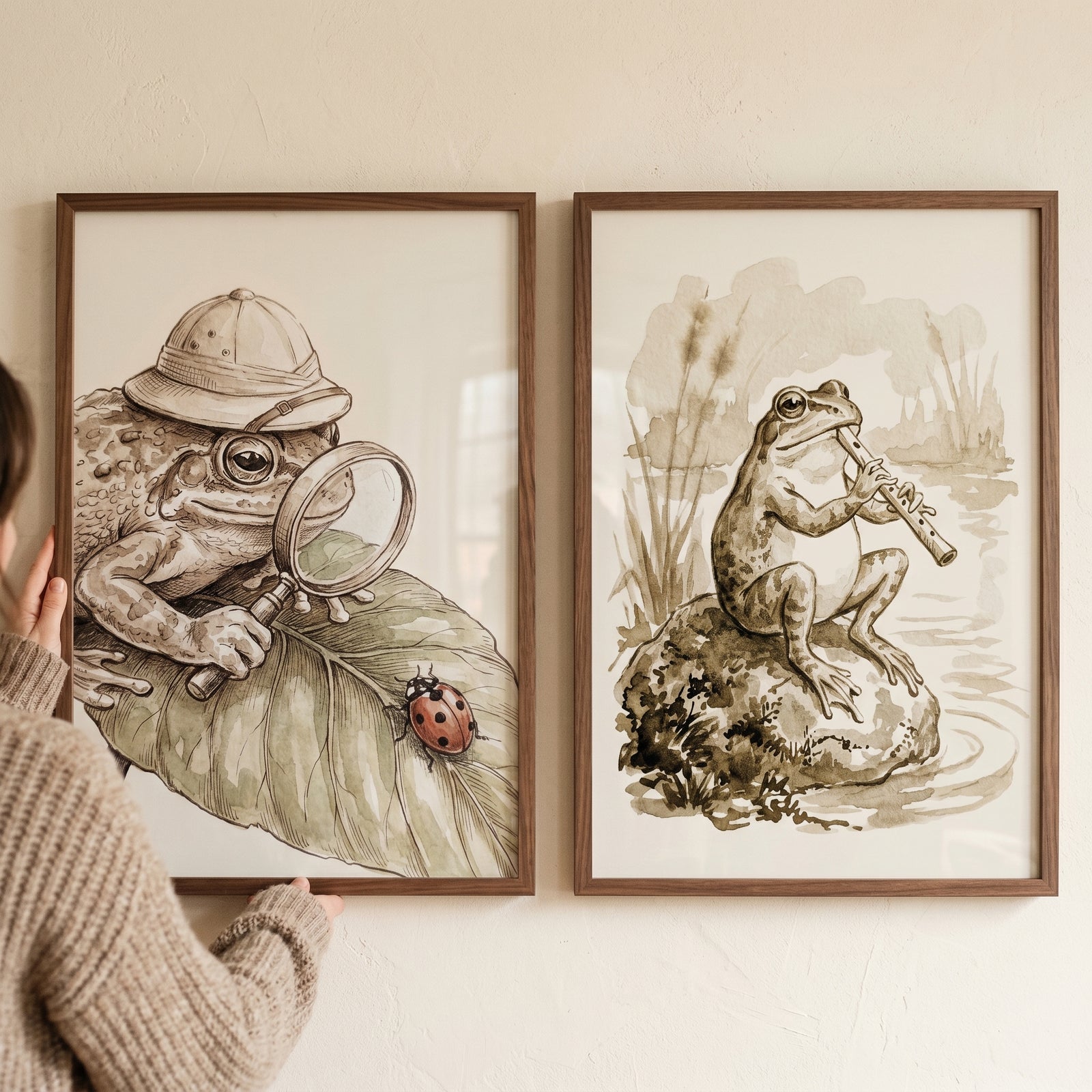 Person holds a vintage sepia storybook frog wall art set of 2 featuring a frog explorer and a frog playing a flute.