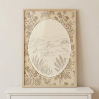 Framed vintage style illustration of two rabbits running across a grassy field, surrounded by delicate floral patterns and an oval border. The soft monochrome tones and detailed linework create a calm and timeless nature inspired print.