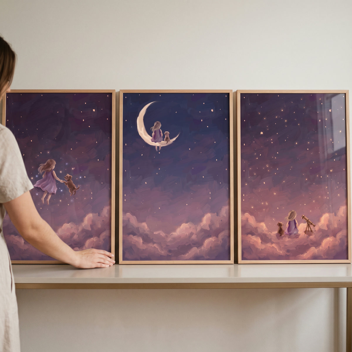 A woman adjusts a violet night girl dog wall art set of 3 on a shelf, showing a girl and dog among stars and clouds.