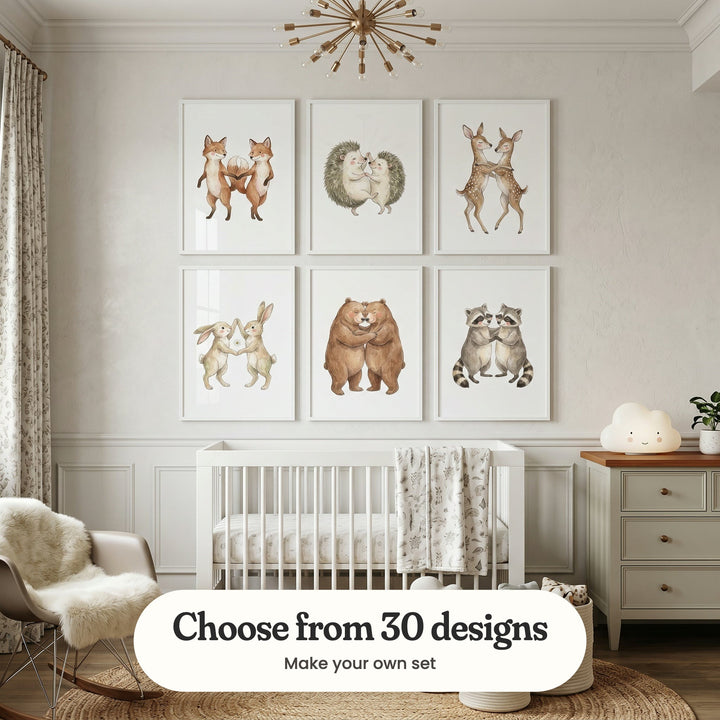 Cream panelled nursery with six animal pair prints in white frames in two rows above a white crib, beside a rocking chair with a sheepskin, a dresser with a cloud lamp and a gold starburst ceiling light: Dancing Fox Duo, Happy Hedgehog Dance, Sweet Fawn Embrace, Dancing Bunny Duo, Gentle Bear Nuzzle and Sweet Raccoon Duo, with a label reading Choose from 30 designs, Make your own set