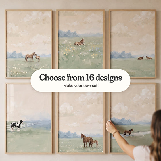 Six peach sky horse prints in light wood frames in two rows, one being straightened by a hand: a mare and foal among white wildflowers, a foal lying in yellow and blue wildflowers, two horses resting in the grass, a black and white horse by a white fence, a brown mare and foal and a horse crossing a stream, with a label reading Choose from 16 designs, Make your own set