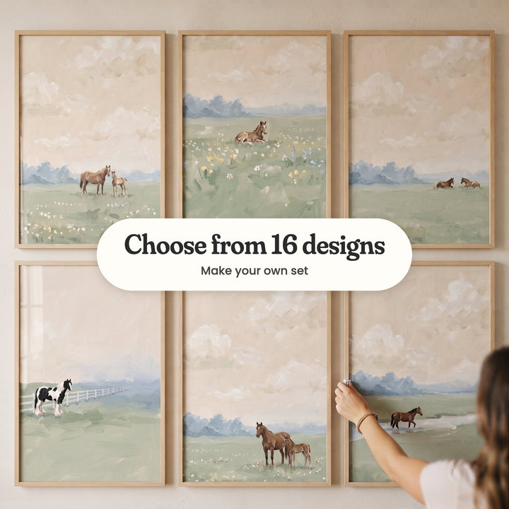 Six peach sky horse prints in light wood frames in two rows, one being straightened by a hand: a mare and foal among white wildflowers, a foal lying in yellow and blue wildflowers, two horses resting in the grass, a black and white horse by a white fence, a brown mare and foal and a horse crossing a stream, with a label reading Choose from 16 designs, Make your own set