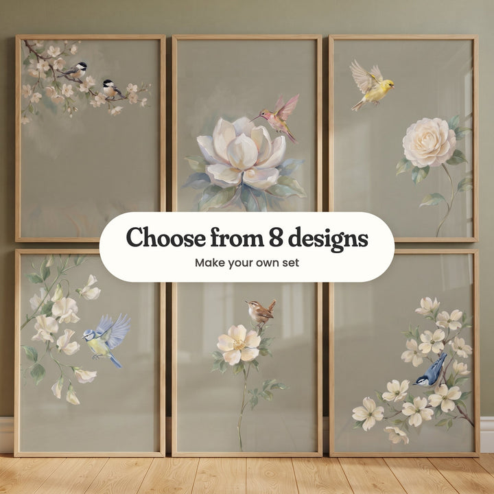 Six songbird prints in light wood frames leaning on the floor in two rows against a sage wall: two chickadees on white blossom, a hummingbird at a magnolia, a yellow finch above a cream bloom, a blue tit by sweet peas, a wren on a wild rose and a nuthatch in dogwood, with a label reading Choose from 8 designs, Make your own set
