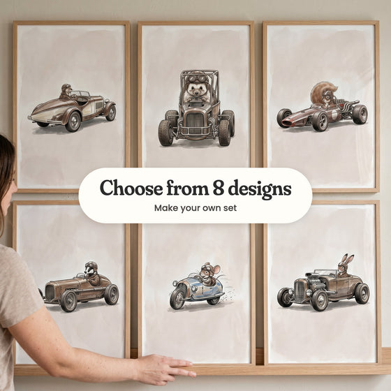 A hand straightening one of six vintage racing prints in light wood frames in two rows on a picture ledge: an otter in a cream and brown speedster, a hedgehog in a hot rod buggy with a roll cage, a squirrel in an open-wheel racer, a badger in a single-seat racer, a mouse in a pale blue racer and a hare in a hot rod with a big chrome engine, with a label reading Choose from 8 designs, Make your own set