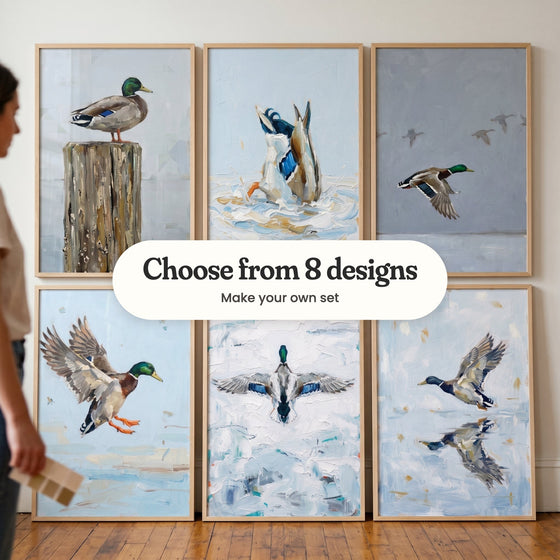 Six mallard duck prints in light wood frames leaning against a wall while a woman holds paint swatches, with a label reading Choose from 8 designs, Make your own set