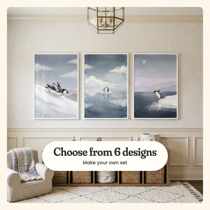 Cream panelled room with three penguin prints in white frames above a low shelf of woven baskets, beside an armchair with a plaid throw, under a brass lantern light: Midnight Snow Slide, Starlit Penguin Duo and Penguin Ice Dive, labeled Choose from 6 designs, Make your own set