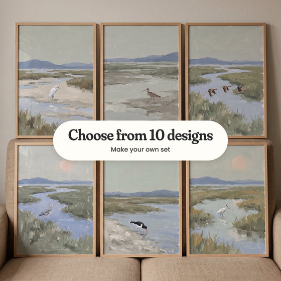 Six marsh bird prints in light wood frames propped on a beige sofa: a white egret on a sandbar, a curlew on the mudflats, three geese in flight, a heron wading under a pink sun, an oystercatcher at the water's edge and a spoonbill under a pink sun, with a label reading Choose from 10 designs, Make your own set