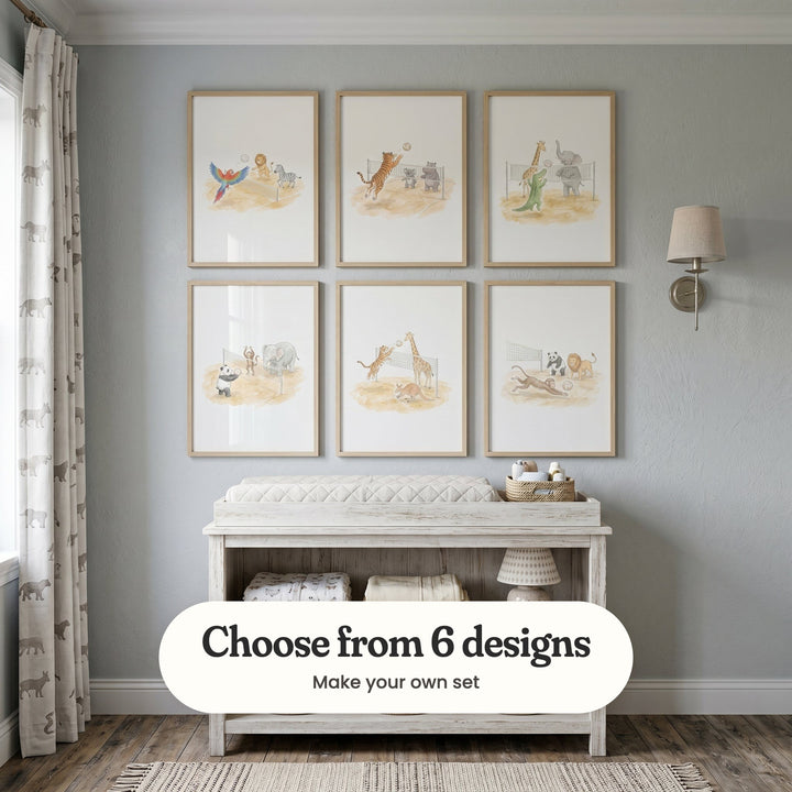 Pale blue grey nursery with six volleyball animal prints in light wood frames in two rows above a whitewashed changing table, beside a wall light and animal print curtains: Safari Sports Match, Wild Volleyball Match, Safari Beach Match, Animal Volleyball Fun, Wild Beach Volley and Beach Volleyball Animals, with a label reading Choose from 6 designs, Make your own set