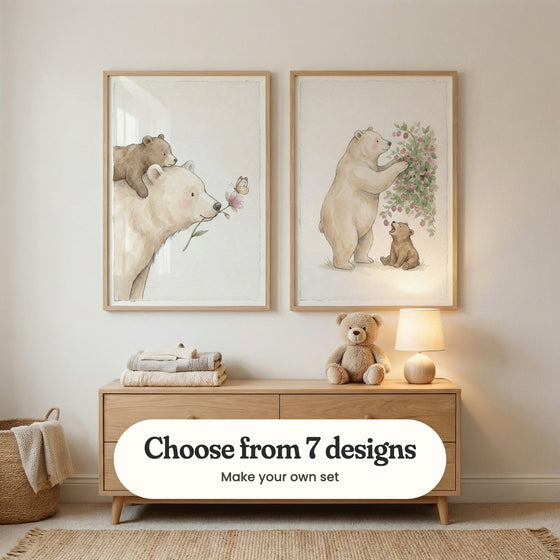 Nursery with two bear and cub prints in light wood frames above a light oak dresser with folded blankets, a plush teddy bear and a small lamp, beside a woven basket and a jute rug: Gentle Bear Bond and Sweet Berry Sharing, with a label reading Choose from 7 designs, Make your own set