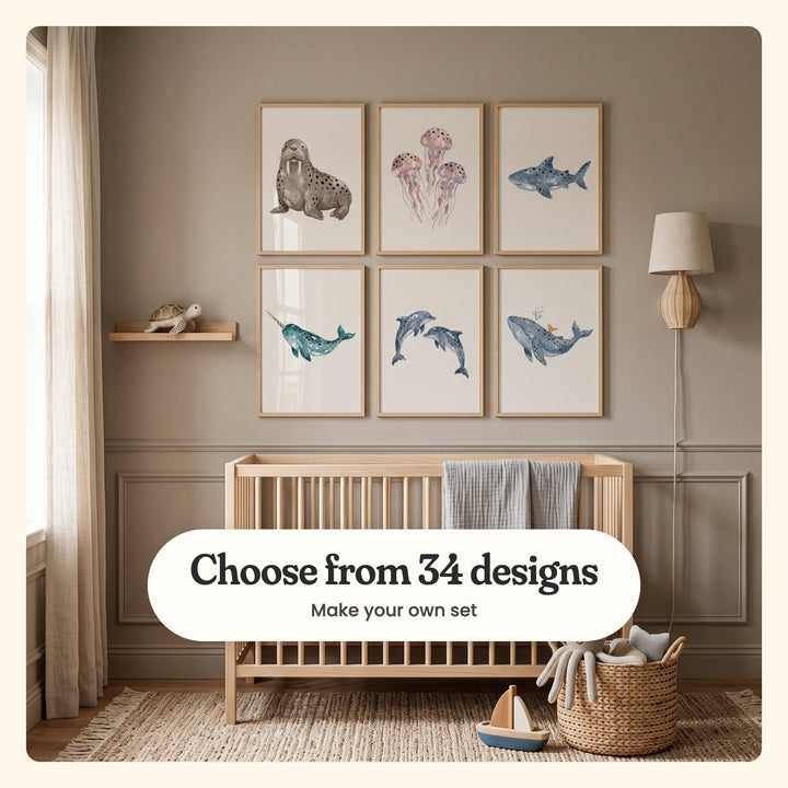 Nursery with six spotted sea animal prints in light wood frames in two rows above a wooden crib with a grey muslin, beside a floating shelf with a wooden turtle, a rattan wall lamp and a woven basket with a plush octopus, with a wooden toy boat on a jute rug: a walrus, three jellyfish, a grey-blue shark, a teal narwhal, two leaping dolphins and a whale with a little bird on its back, labeled Choose from 34 designs, Make your own set