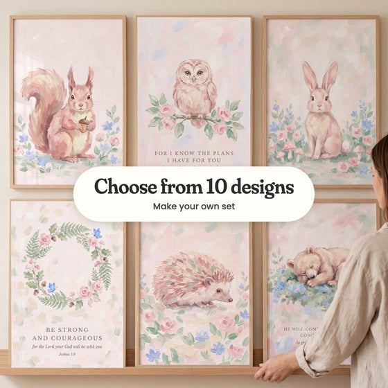Six blush woodland prints in light wood frames in two rows, one held by a hand in a linen sleeve: a squirrel holding an acorn, an owl on a rose branch with a Bible verse, a bunny among flowers and mushrooms, a fern and rose wreath with the verse Be strong and courageous, a hedgehog among roses and a sleeping bear cub, with a label reading Choose from 10 designs, Make your own set