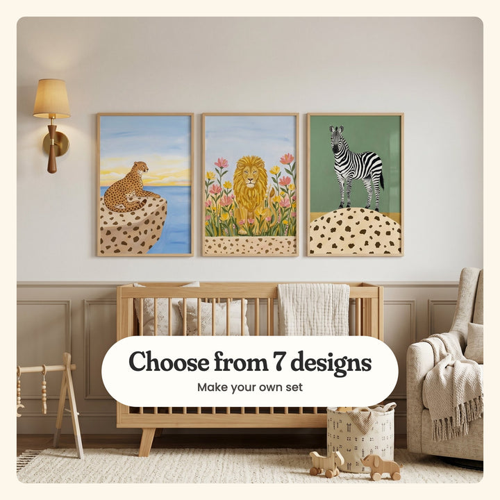 Nursery with three safari animal prints in light wood frames above a light wood crib with a muslin blanket, beside a brass wall sconce, a wooden baby play gym, a cream armchair with a knit throw and a toy basket on a cream rug: a cheetah on a spotted rock by the sea, a lion among pink and yellow flowers and a zebra on sage green, labeled Choose from 7 designs, Make your own set