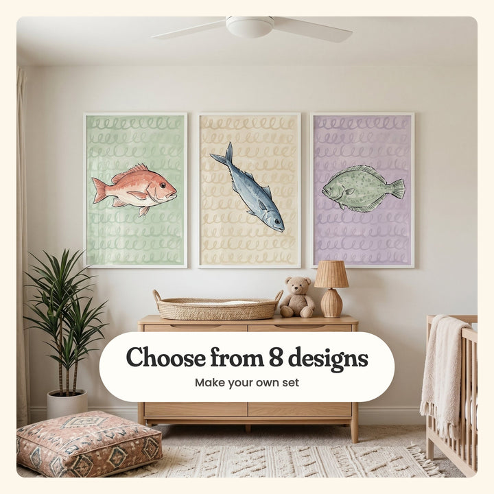 Cream nursery with three fish prints in white frames above a light wood dresser with a woven basket, a teddy bear and a lamp, beside a potted palm, a floor cushion and a crib: Red Snapper Swirls, Silver Sea Swirls and Lavender Sea Flounder, labeled Choose from 8 designs, Make your own set