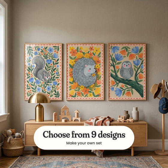 Kids' room with three woodland animal prints in light wood frames above an oak console with a brass lamp, wooden blocks and a rust throw, beside a coat stand with hats and a basket of plush toys: Whimsical Squirrel Garden, Floral Forest Friend and Whimsical Forest Owl, with a label reading Choose from 9 designs, Make your own set