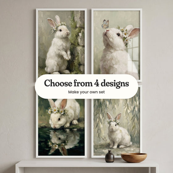 Four white bunny prints in white frames in two rows on a grey wall above a white console with a dark vase and a wooden bowl: a bunny standing by a mossy stone wall, a bunny with a blue butterfly on its nose, a bunny drinking from a dark pond and a bunny under willow branches, with a label reading Choose from 4 designs, Make your own set
