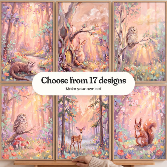 Six sunbeam forest prints in light wood frames in two rows on a wood ledge, one steadied by a hand in a knit sleeve: an otter by a stream, a bunny by a tree with a little door, an owl on a birch branch, an owl above red mushrooms, a fawn among tall pines and a squirrel among flowers, with a label reading Choose from 17 designs, Make your own set