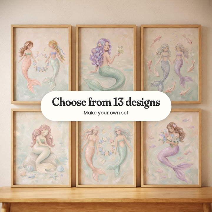 Six mermaid prints in light wood frames in two rows leaning on a wood bench: two mermaids holding a flower wreath, a lavender-haired mermaid with a butterfly on her hand, two mermaids among pink fish, a rose-haired mermaid sitting on a rock, a peach-tailed and a mint-tailed mermaid by a wreath, and a mermaid hugging a bouquet, with a label reading Choose from 13 designs, Make your own set