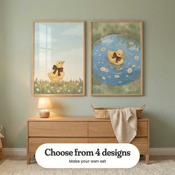 Sage green room with two duckling prints in light wood frames above a light wood dresser with a table lamp and a woven basket with a muslin blanket: Sweet Ribbon Duck and Little Bow Duckling, with a label reading Choose from 4 designs, Make your own set