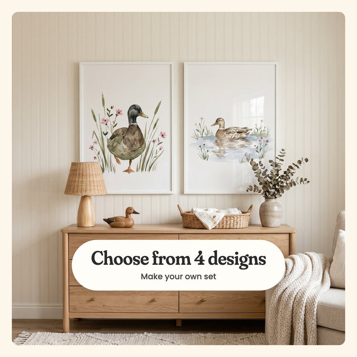 Beadboard wall with two duck prints in white frames above an oak dresser with a rattan lamp, a wooden duck decoy, a woven basket of muslin and eucalyptus in a vase, beside an armchair with a knit throw: a mallard walking through cattails and a brown duck floating on a pond, labeled Choose from 4 designs, Make your own set