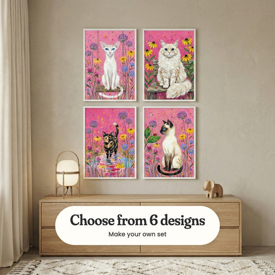 Beige room with four cat prints in white frames in two rows above a low light wood dresser with a lantern lamp and a wooden elephant: Enchanted Garden Feline, Sunlit Garden Cat, Pink Petal Puddle and Floral Feline Gaze, with a label reading Choose from 6 designs, Make your own set