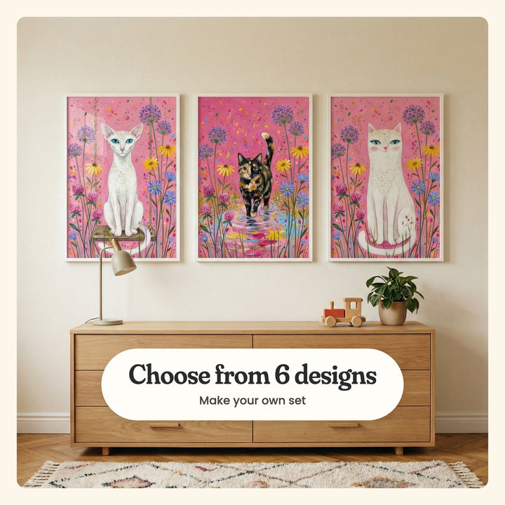 Cream room with three cat prints in white frames above a light wood dresser with a desk lamp, a toy train and a plant, on a patterned rug: Enchanted Garden Feline, Pink Petal Puddle and Pink Garden Cat, labeled Choose from 6 designs, Make your own set