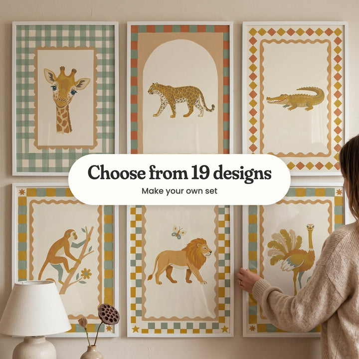 Six safari animal prints in white frames in two rows, with a woman holding one and a lamp and a dried lotus pod in front: a giraffe inside a sage gingham border, a leopard walking under an arch, a crocodile inside a diamond border, a monkey climbing a branch, a lion walking with a butterfly and an ostrich with fanned feathers, with a label reading Choose from 19 designs, Make your own set