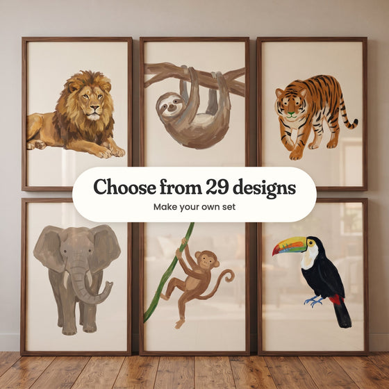 Six animal prints in walnut frames in two rows leaning on a wood floor against a taupe wall: a lion lying down, a sloth hanging from a branch, a tiger walking, an elephant, a monkey swinging on a vine and a toucan, with a label reading Choose from 29 designs, Make your own set