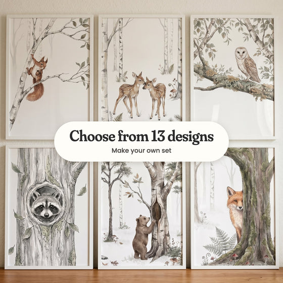 Six woodland animal prints in white frames on a wooden ledge: a red squirrel on a birch branch, two fawns nuzzling, a barn owl, a raccoon in a tree hollow, a bear cub at a hollow birch and a fox peeking from behind a tree, with a label reading Choose from 13 designs, Make your own set