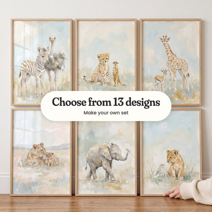 Six animal prints in light wood frames in two rows against a white wall, with a hand in a cream knit sleeve: a zebra foal and an ostrich, a cheetah cub and a meerkat, a young giraffe and a gazelle, a lioness and her cub, a baby elephant with a bird on its trunk and a lion cub with a little bird, with a label reading Choose from 13 designs, Make your own set