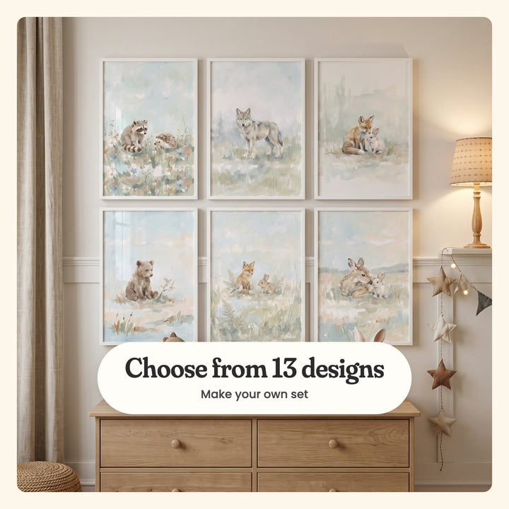 Nursery with six animal prints in white frames in two rows above an oak dresser, beside star bunting, a linen curtain and a woven pouf: a raccoon and a hedgehog, a lone wolf in misty grass, a fox cub nuzzling a bunny, a bear cub with a little bird, a fox cub, bunny and bird among ferns and a fawn lying with a bunny, labeled Choose from 13 designs, Make your own set