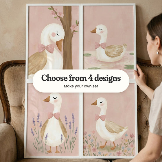 Four goose prints in white frames held up against the back of a tan tufted sofa by a woman, each goose wearing a pink polka-dot bow, with a label reading Choose from 4 designs, Make your own set
