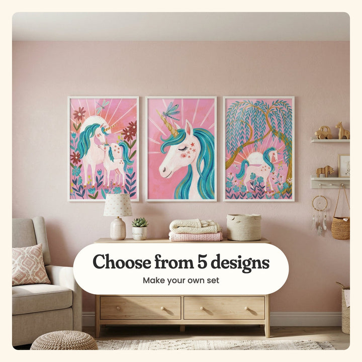 Blush pink nursery with three unicorn prints in white frames above a light wood dresser with a lamp, a small plant and folded blankets, beside an armchair, a pouf and wall shelves with wooden toys: Magical Unicorn Duo, Starlit Unicorn Gaze and Golden Willow Unicorn, labeled Choose from 5 designs, Make your own set
