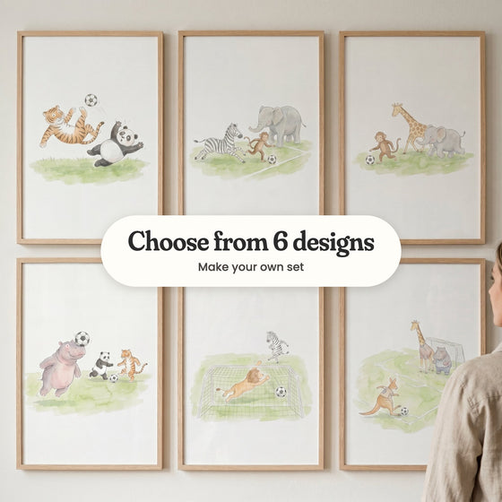Six safari animal soccer prints in light wood frames in two rows on a pale wall: a tiger's bicycle kick over a panda, a zebra, monkey and elephant chasing the ball, a monkey dribbling past a giraffe and elephant, a hippo heading the ball, a lion goalkeeper diving and a kangaroo shooting at goal, with a label reading Choose from 6 designs, Make your own set