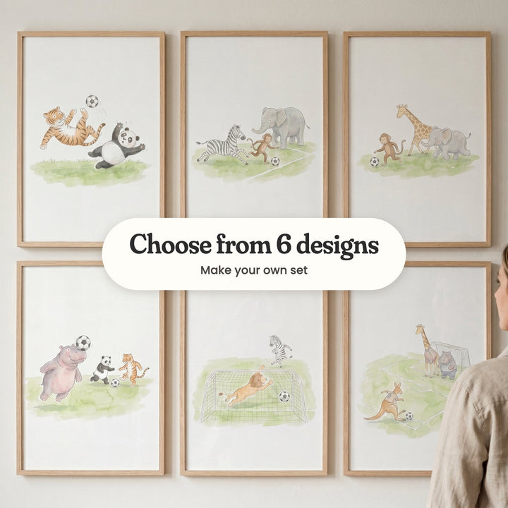 Six safari animal soccer prints in light wood frames in two rows on a pale wall: a tiger's bicycle kick over a panda, a zebra, monkey and elephant chasing the ball, a monkey dribbling past a giraffe and elephant, a hippo heading the ball, a lion goalkeeper diving and a kangaroo shooting at goal, with a label reading Choose from 6 designs, Make your own set