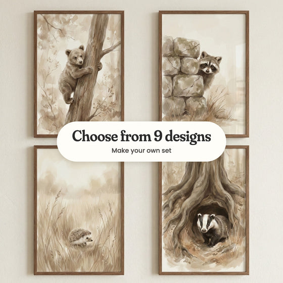 Four woodland animal prints in dark wood frames on a cream wall: a bear cub climbing a tree, a raccoon peeking around a stone wall, a hedgehog in tall grass and a badger in its burrow, with a label reading Choose from 9 designs, Make your own set