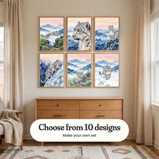 Nursery with six snow leopard prints in light wood frames in two rows above a wood dresser between cream curtains, beside a chair with a knit throw: Snow Leopard Leap, Snowy Mountain Gaze, Silent Mountain Guardian, Mountain Ghost Ascent, Silent Mountain Watcher and Silent Snow Stride, with a label reading Choose from 10 designs, Make your own set