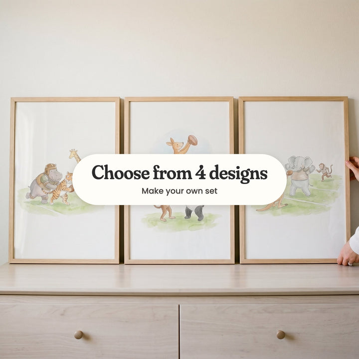 Three safari animal football prints in light wood frames leaning on a pale wood dresser: a hippo in a helmet and a tiger with the ball racing past a giraffe, a kangaroo leaping for the ball lifted by a monkey and a panda, and a kangaroo tossing the ball to an elephant, with a label reading Choose from 4 designs, Make your own set
