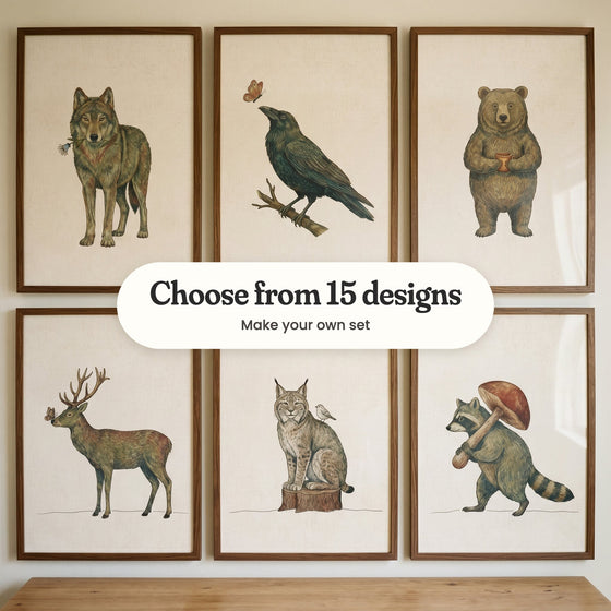 Six woodland animal prints in dark wood frames on a wall: a wolf with a blue flower, a raven, a bear holding a mug, a buck with a butterfly on its nose, a lynx on a stump and a raccoon carrying a mushroom, with a label reading Choose from 15 designs, Make your own set
