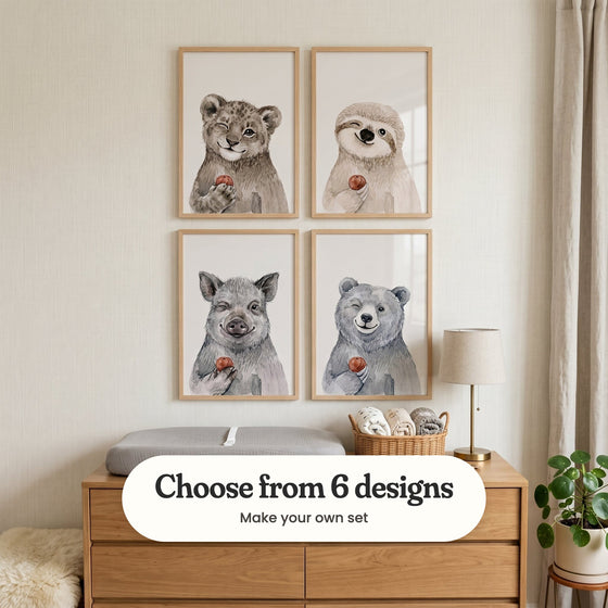 Cream nursery with four animal prints in light wood frames in two rows above a light wood changing dresser with a grey changing pad, a basket of rolled towels and a lamp, beside a sheepskin and a potted plant: Winking Jungle Cub, Winking Sloth Friend, Winking Wild Boar and Winking Forest Bear, with a label reading Choose from 6 designs, Make your own set