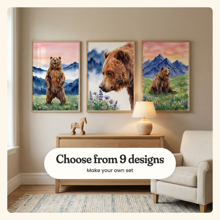 Three bear prints in light wood frames above an oak dresser with a wooden toy horse and a ceramic lamp, beside a cream armchair and a window on a striped blue rug: a bear standing on its hind legs in a meadow, a close-up bear sniffing purple lupines and a bear sitting in a wildflower meadow under purple peaks, labeled Choose from 9 designs, Make your own set