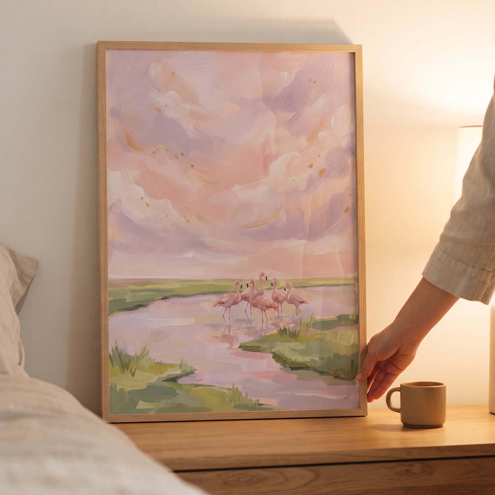 Wading blush pink flamingo animal wall art in a wood frame on a nightstand depicts birds in a marsh under a pastel sky.