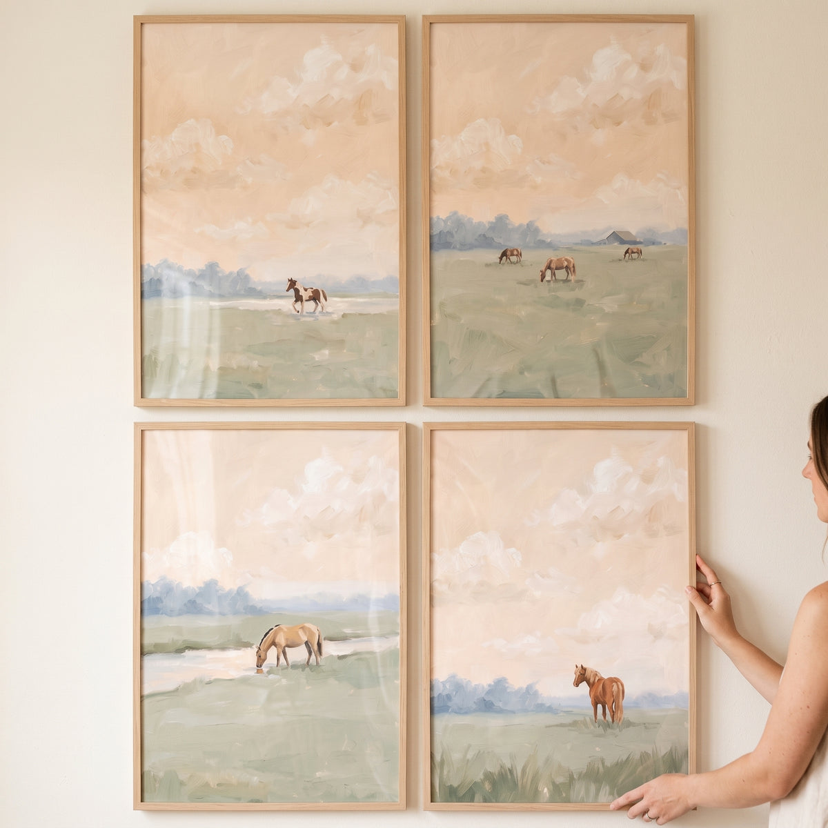 A person holds a warm dusk meadow horse wall art set of 4 against a wall, showing horses in soft, golden landscapes.