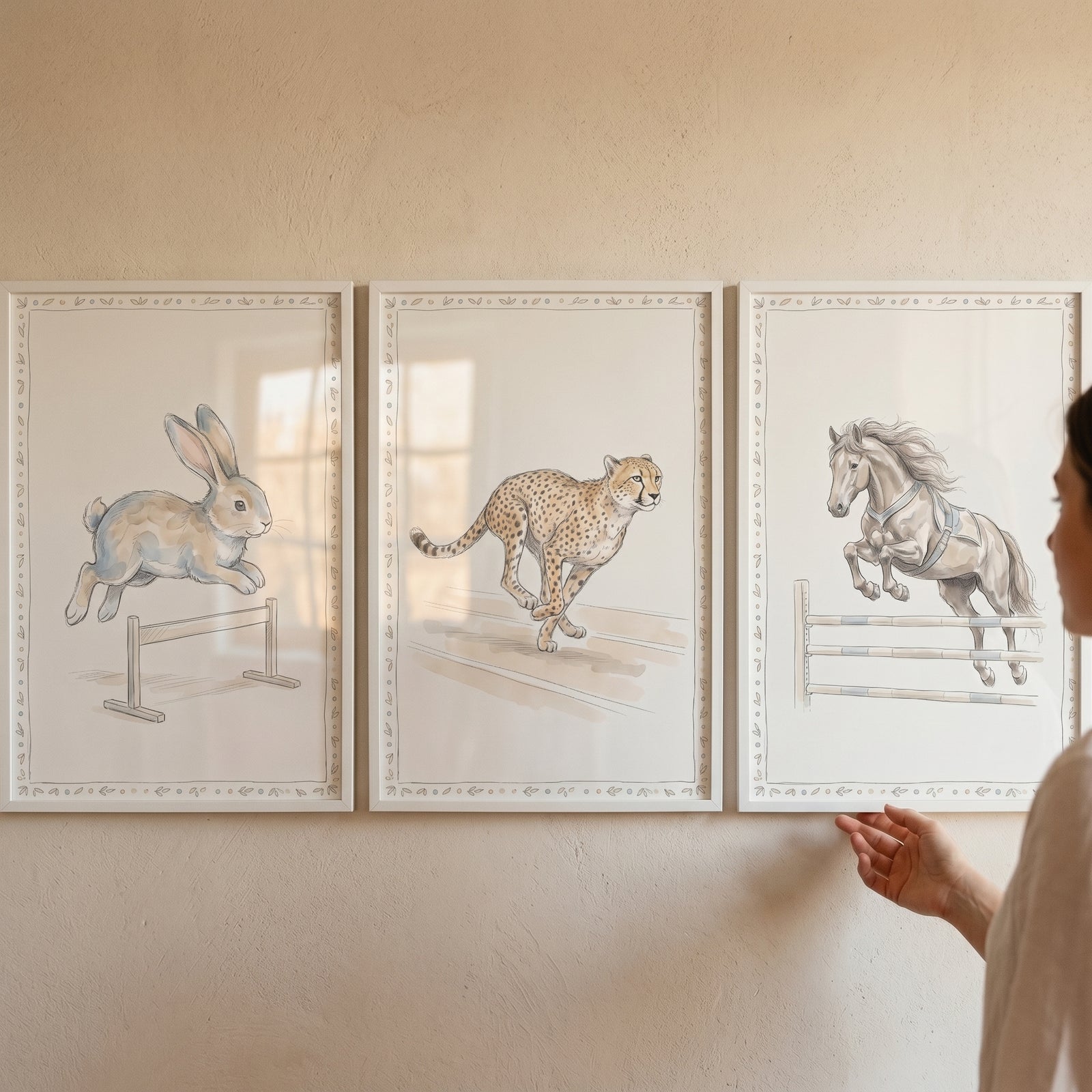A woman adjusts a watercolor athletic animal wall art set of 3 featuring a jumping rabbit, running cheetah, and horse.