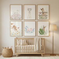 A serene nursery scene featuring a light-toned wooden crib centered under six framed illustrations on a neutral wall. The art depicts various baby farm animals in a soft watercolor style: a lamb, an alpaca with a flower crown, a horse behind a fence, a brown and white calf, a pink piglet among blue flowers, and a rabbit behind a large green leaf. To the left of the crib is a woven basket filled with toys, and to the right stands a minimalist floor lamp with a gold base and a cream-colored shade.