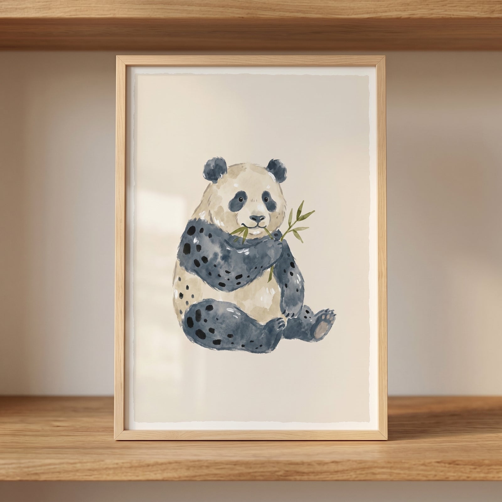 Framed watercolor bamboo eating panda wall art rests on a light wooden shelf in a neutral room.