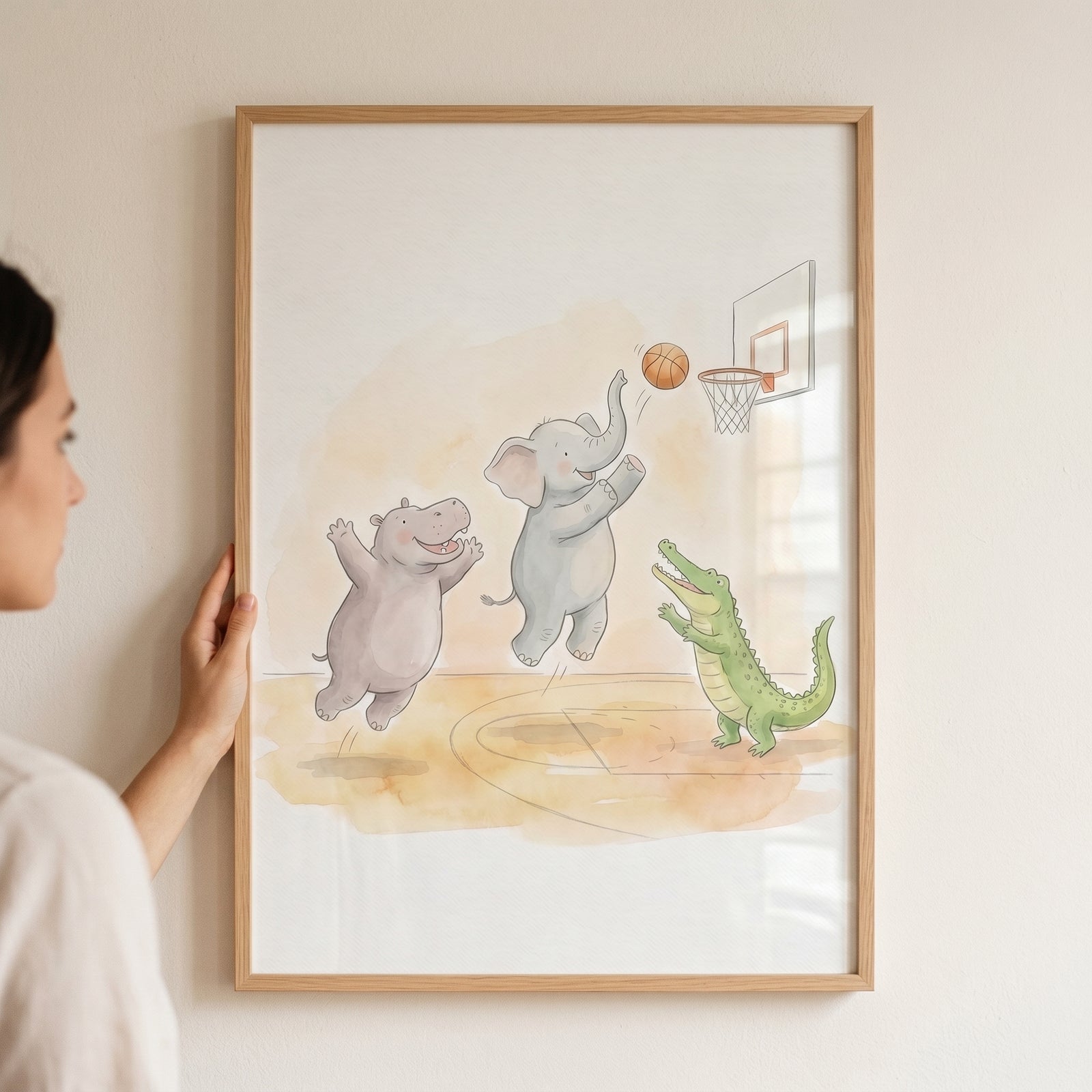 Person holds framed watercolor basketball safari animals wall art of a hippo, elephant, and crocodile.